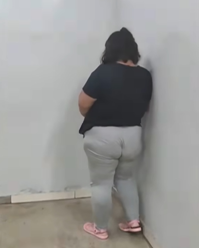 A woman in a black shirt and light pants stands facing a corner, as she learns her fate in court.
