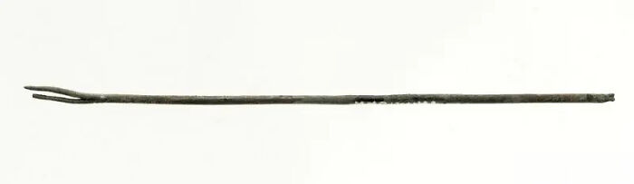 A thin, dark historical artifact resembling a two-pronged fork or tool, a testament to its survival against the odds.