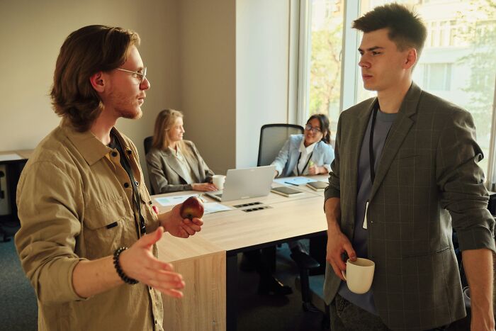 Two men in an office, one holding an apple, delivering sick burns during a conversation.