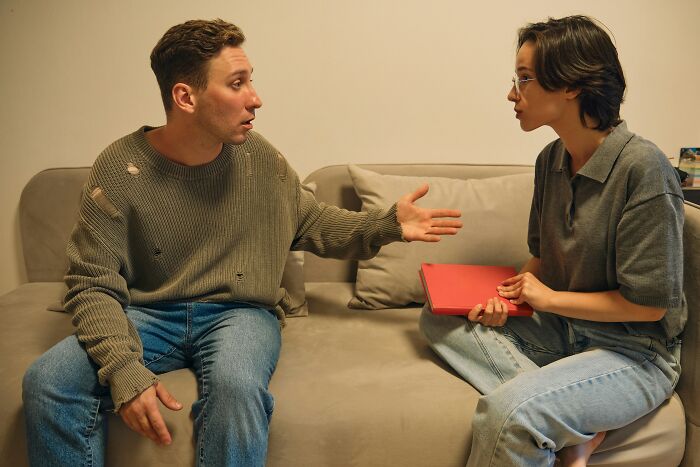 A couple arguing on a couch, with the boyfriend gesturing, reflecting a moment he said something regrettable.
