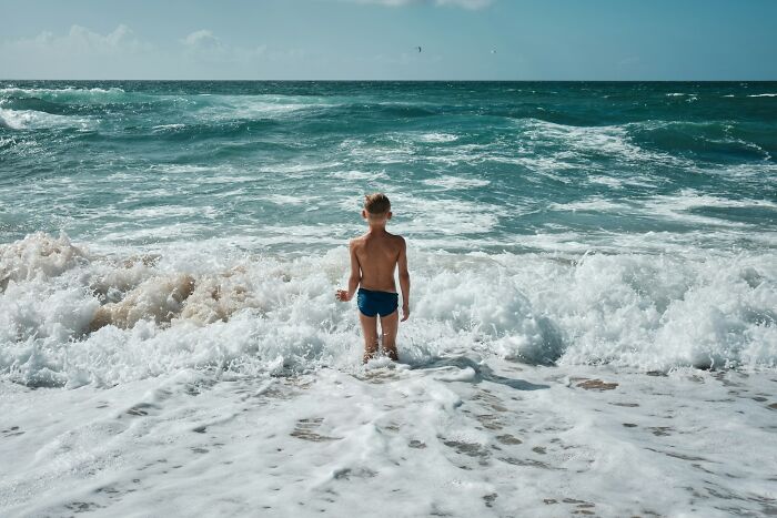 Young boy standing in ocean waves alone, a potential scenario with a horrible parent.