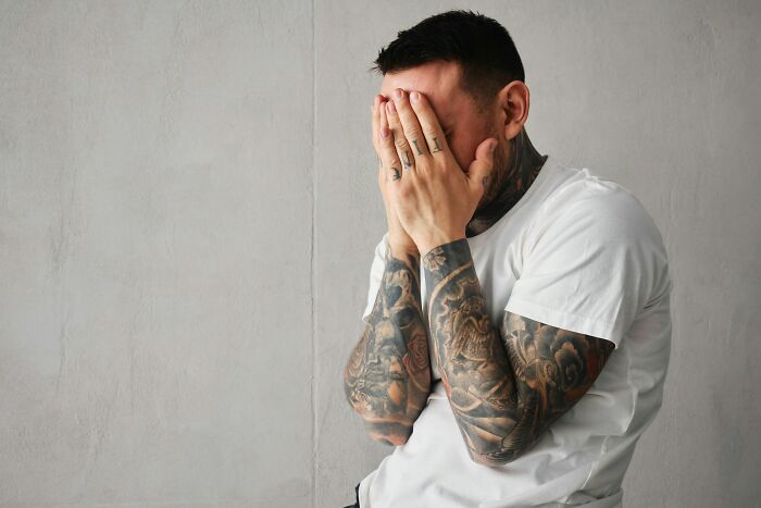 A man with tattoos covers his face with his hands, realizing he's with the wrong person.