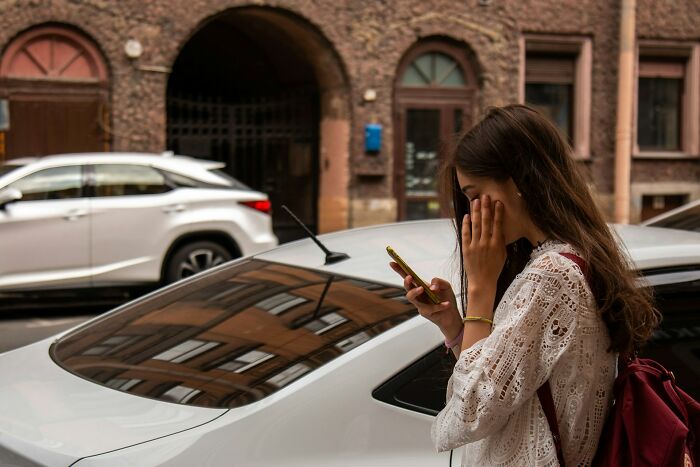 A woman looking at her phone with a hand to her face, possibly reacting to breakup-worthy things her partner did.