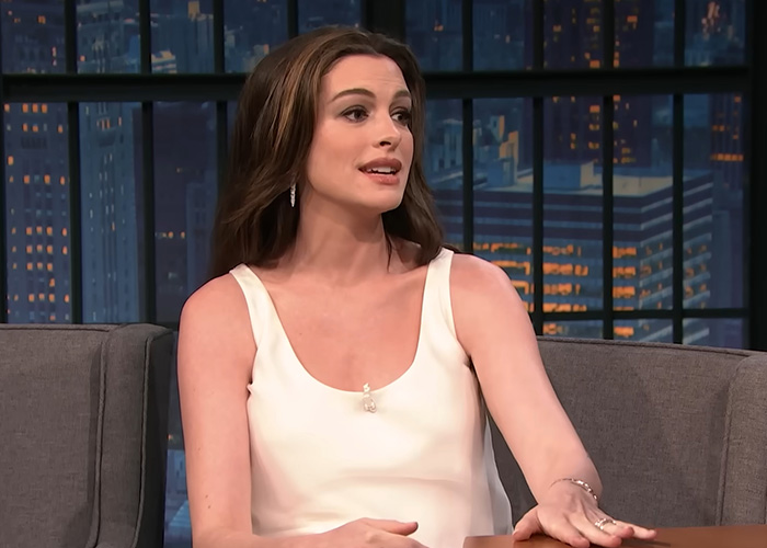 Anne Hathaway, not pregnant, in a white top, seated and talking during an interview.