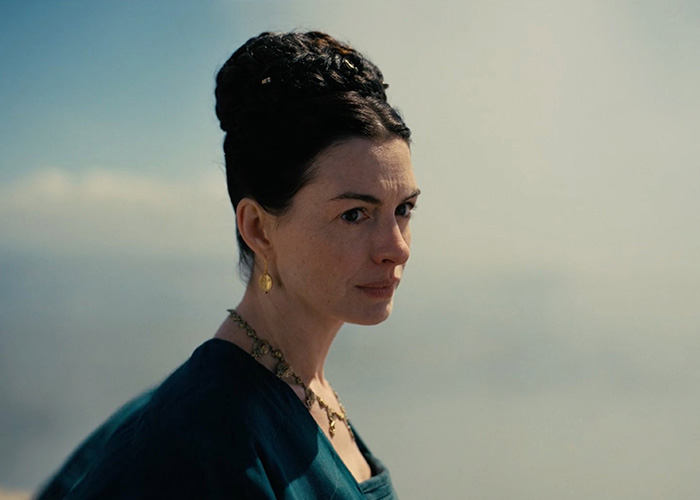 Anne Hathaway in character, looking contemplative against a hazy sky, wearing an elegant dress.