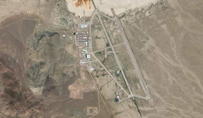 Aerial view of Area 51, revealing its secretive layout with runways and buildings, fueling theories beyond aliens and UFOs. Aerial view of Area 51, revealing its secretive layout with runways and buildings, fueling theories beyond aliens and UFOs.