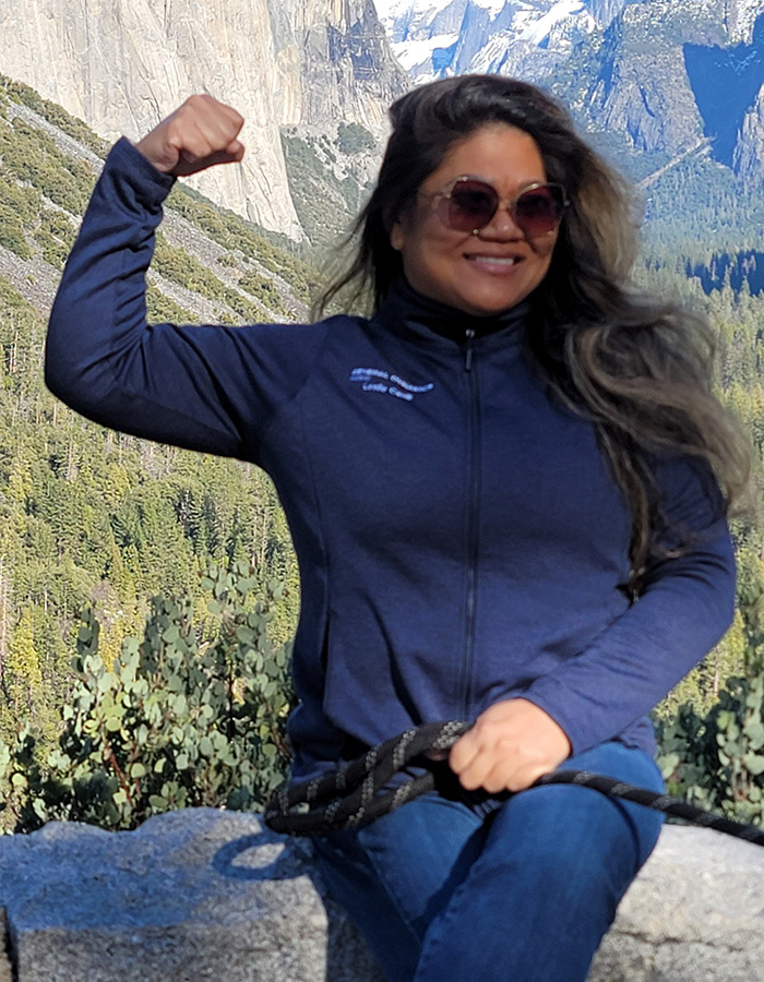 A strength athlete, 41, poses flexing her arm in front of a mountain landscape before losing arms and legs.