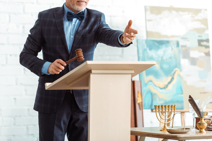 An auctioneer with a gavel at a podium during a charity auction, ready to announce a bid. An auctioneer with a gavel at a podium during a charity auction, ready to announce a bid.