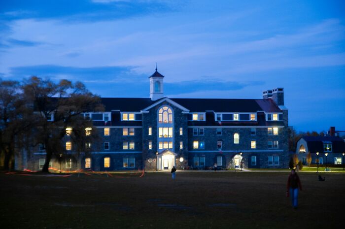 College life building at dusk with students on the lawn, showing the freedom and new world of university.