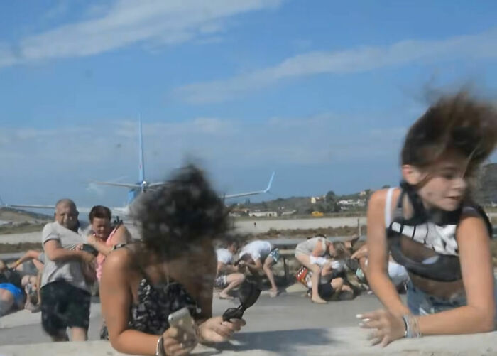 People reacting to a plane's jet engine blast, showing the woman being slammed to the ground.