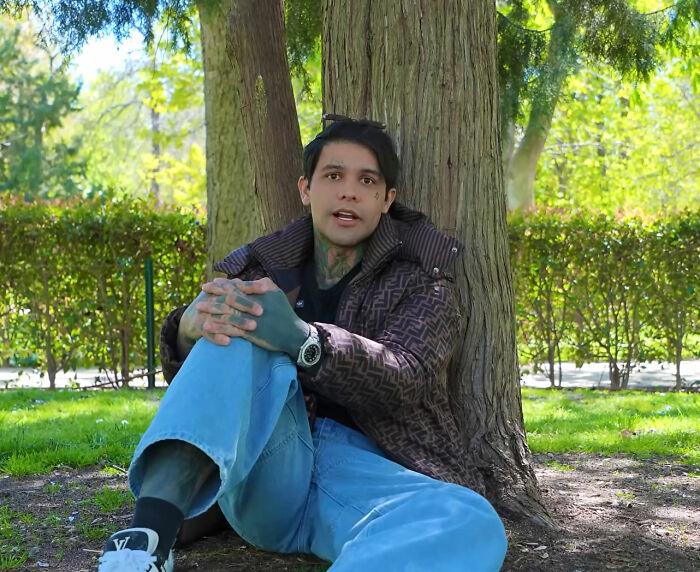 An influencer with tattoos sitting under a tree, reflecting on his mid-flight prank.