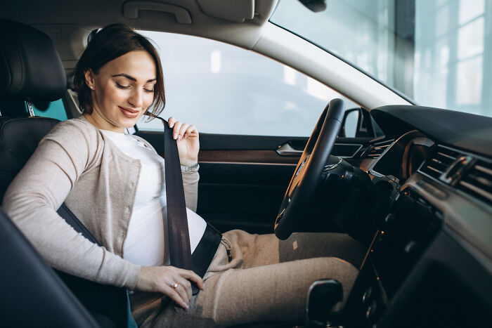 A pregnant woman in a car fastening her seatbelt, a sign from the universe for safety and new beginnings.