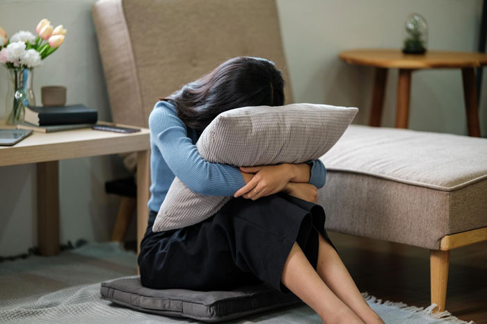 A heartbroken bestie sitting on the floor, holding a pillow and looking upset. A heartbroken bestie sitting on the floor, holding a pillow and looking upset.
