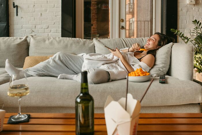 A woman happily lounging on a couch, eating snacks and watching TV, enjoying being single and living alone.