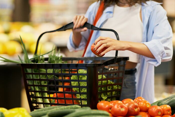 A woman placing a tomato into a shopping basket, representing independence while living alone.