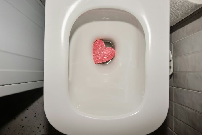 A pink heart-shaped toilet cleaner in a toilet bowl, symbolizing moving on from past relationships and loving being single.