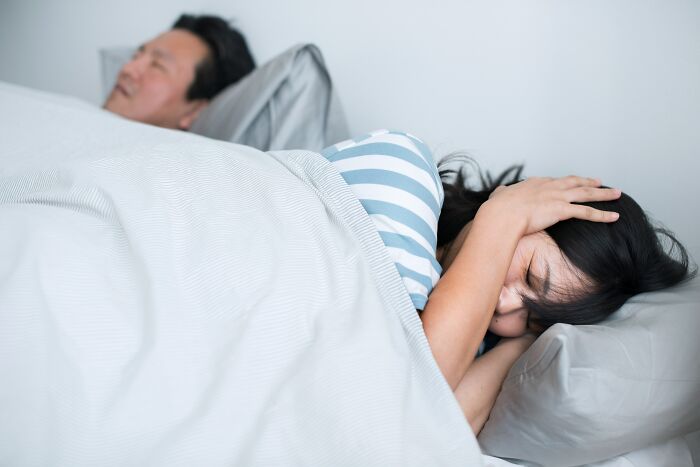 A woman covers her ears in bed next to a man, suggesting she secretly loves being single.