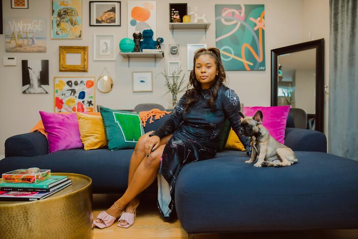 A woman sits on a couch with her small dog, enjoying being single and living alone.