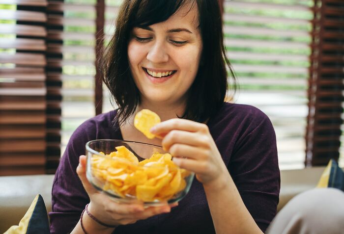 A woman happily eating potato chips from a bowl, highlighting the simple pleasures of living alone and being single.