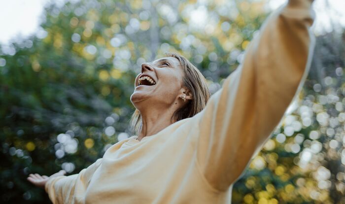 A joyful woman with outstretched arms looks up at the sky, celebrating her freedom and happiness being single.