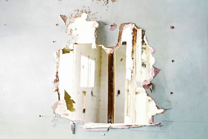 A damaged wall with peeling paint and a hole, reflecting the potential downsides or past struggles before loving being single.