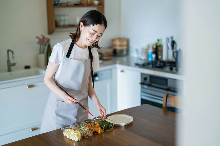 A woman in an apron happily prepares food in her kitchen, embodying the joy of living alone.