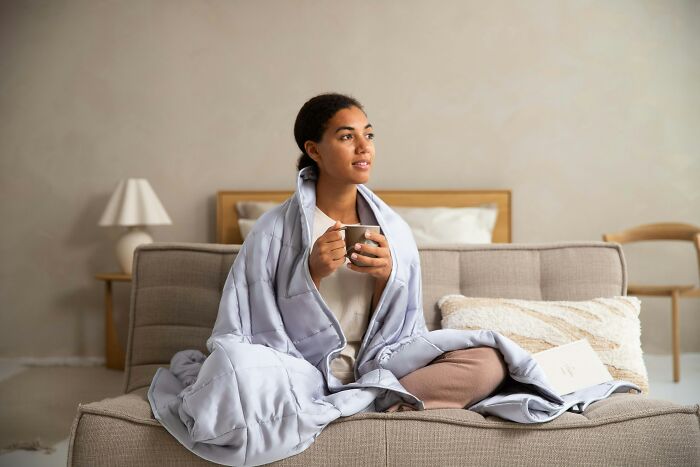 A woman wrapped in a blanket, enjoying a hot drink while living alone in her home.