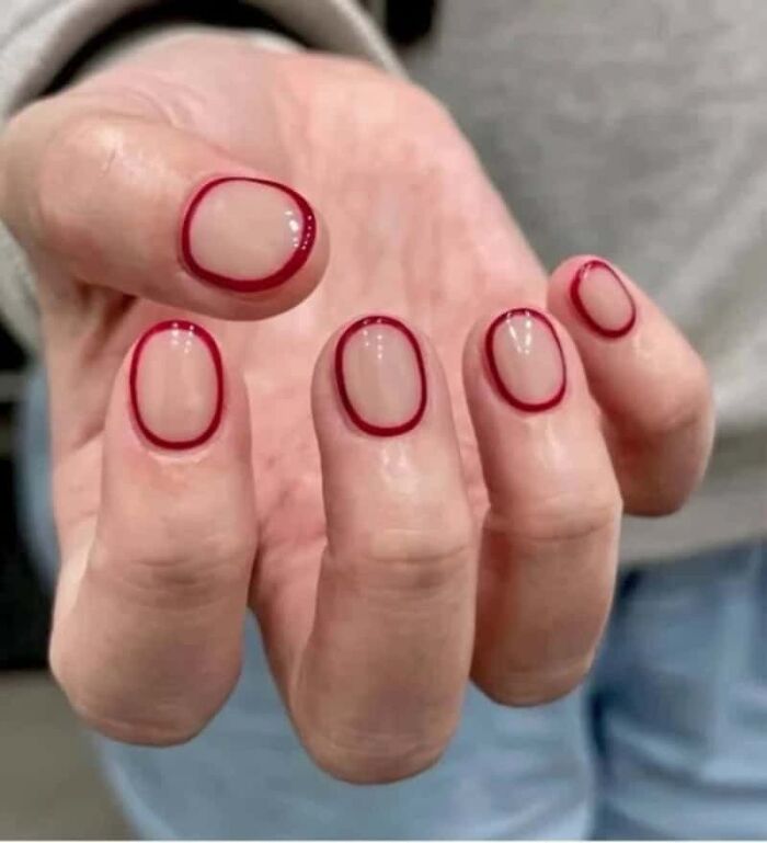 A hand displays disturbing, clear nails with red outline designs, an awful idea executed with skill.