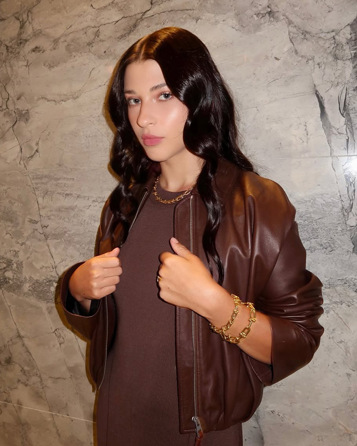 Bill Gates daughter in a brown leather jacket and dress, facing fraud accusations.