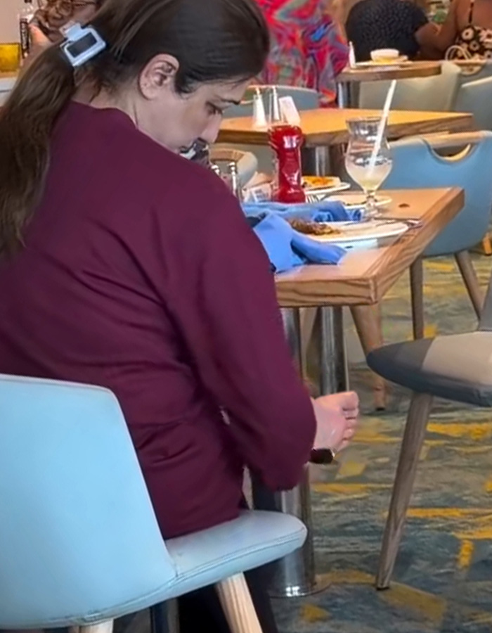 A woman at a restaurant table on a cruise ship, using her foot to open a bottle, a bizarre cruise ship incident.