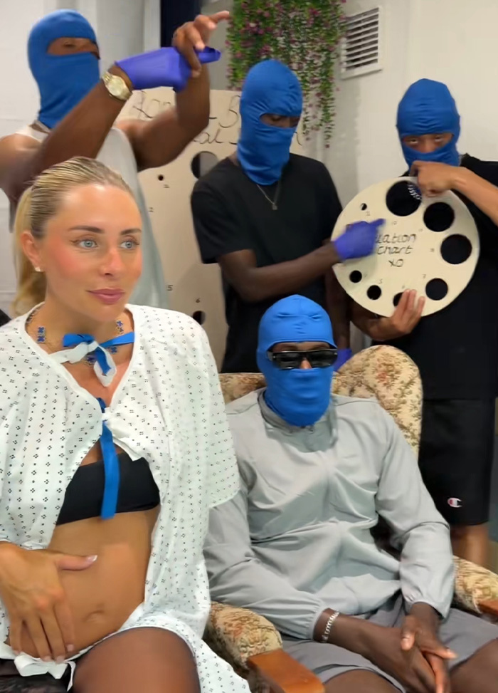 Bonnie Blue, pregnant and wearing a hospital gown, sits next to a man in a blue balaclava, as others with balaclavas hold props related to her Final Stretch stunt. Bonnie Blue, pregnant and wearing a hospital gown, sits next to a man in a blue balaclava, as others with balaclavas hold props related to her Final Stretch stunt.