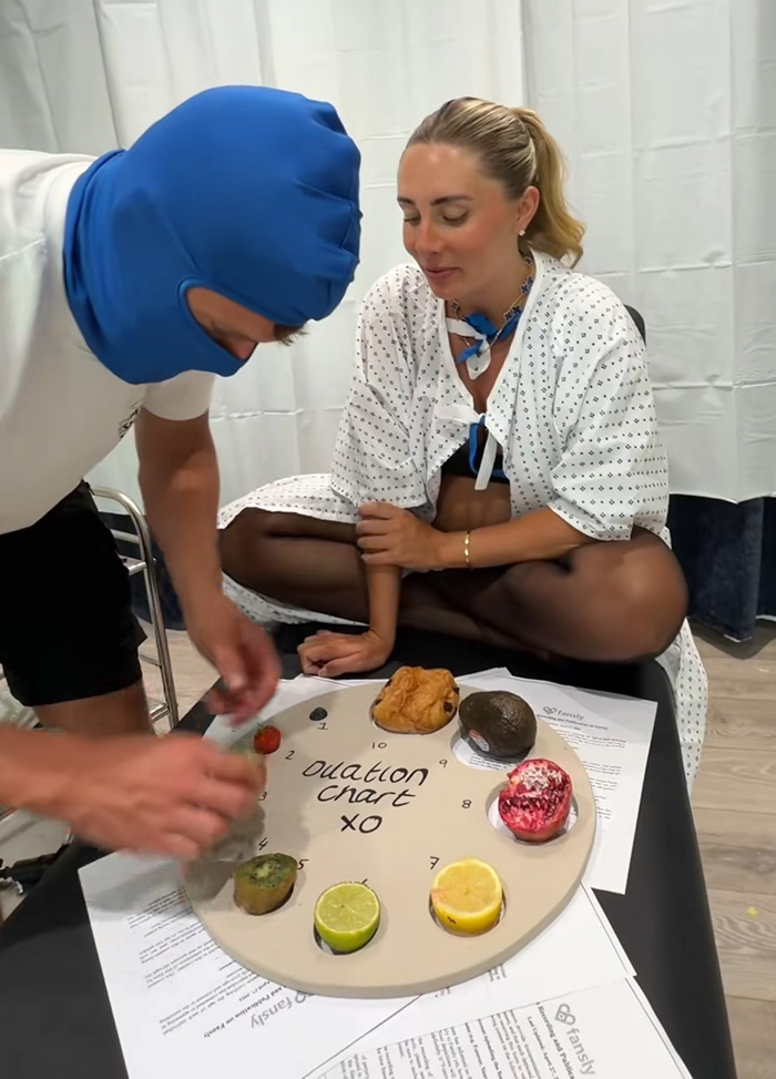 Bonnie Blue observing a man in a blue balaclava placing items on an ovulation chart during a stunt. Bonnie Blue observing a man in a blue balaclava placing items on an ovulation chart during a stunt.