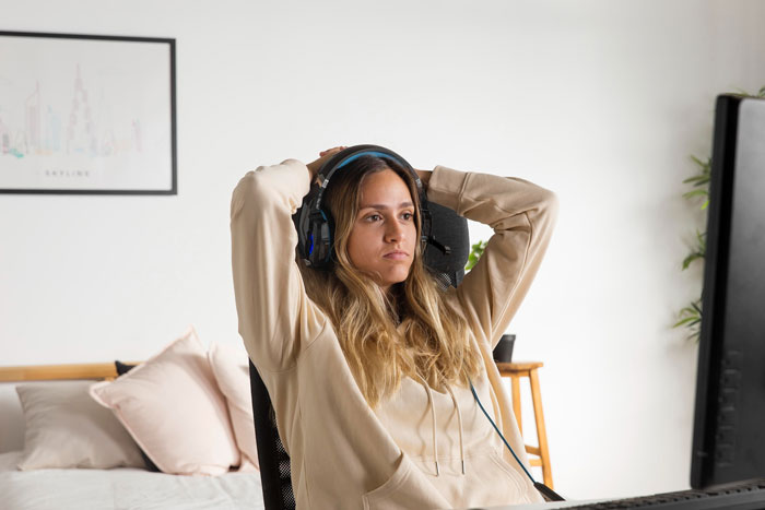 A woman wearing headphones and a beige hoodie, relaxing at a desk, playing friends against each other. A woman wearing headphones and a beige hoodie, relaxing at a desk, playing friends against each other.