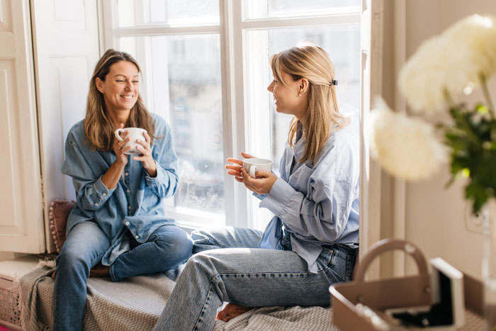 Two friends laughing and enjoying coffee by a window, a contrast to the man playing friends against each other. Two friends laughing and enjoying coffee by a window, a contrast to the man playing friends against each other.