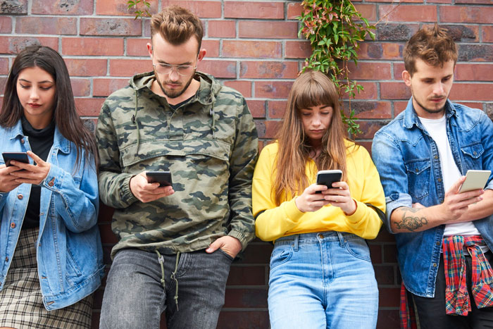 Four young friends focused on their phones against a brick wall, after ex-girlfriend sends receipts. Four young friends focused on their phones against a brick wall, after ex-girlfriend sends receipts.