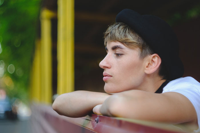 A young person with short hair and a black hat looking thoughtfully into the distance, pondering a relationship unravels. A young person with short hair and a black hat looking thoughtfully into the distance, pondering a relationship unravels.