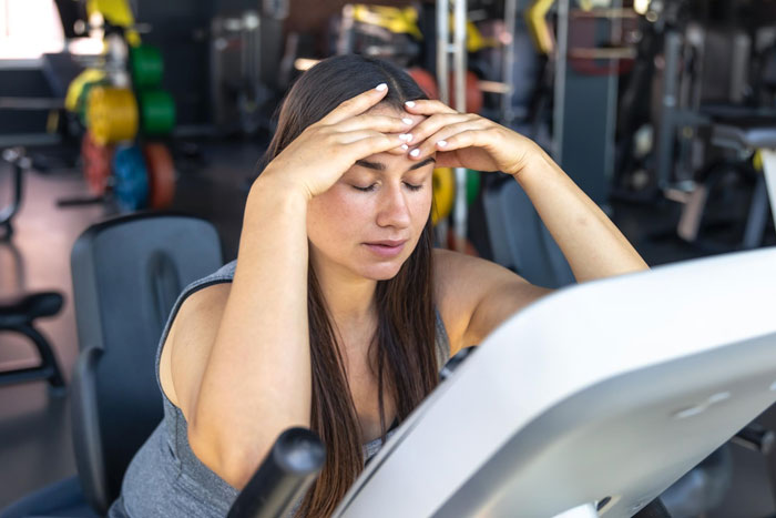 A woman looking tired and stressed in a gym, trying to fix her body because her boyfriend calls her chubby. A woman looking tired and stressed in a gym, trying to fix her body because her boyfriend calls her chubby.