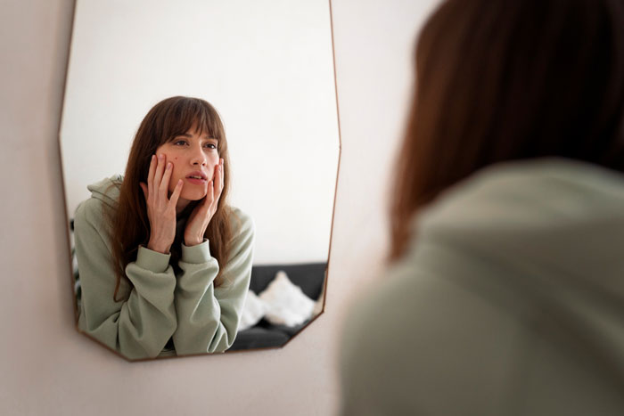 A woman looking distressed in a mirror, possibly feeling self-conscious after her boyfriend called her chubby and tried to fix her. A woman looking distressed in a mirror, possibly feeling self-conscious after her boyfriend called her chubby and tried to fix her.