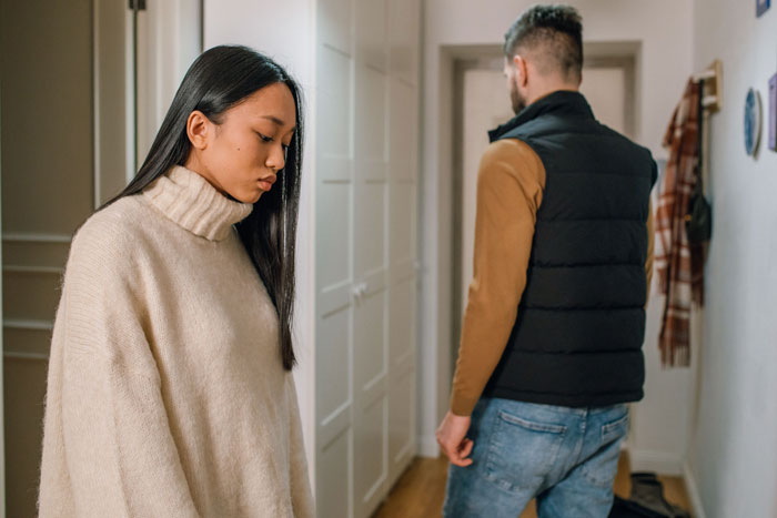 A woman with long dark hair, looking downcast, stands in a hallway while a man with his back turned walks away, showing the dream girl and guy. A woman with long dark hair, looking downcast, stands in a hallway while a man with his back turned walks away, showing the dream girl and guy.