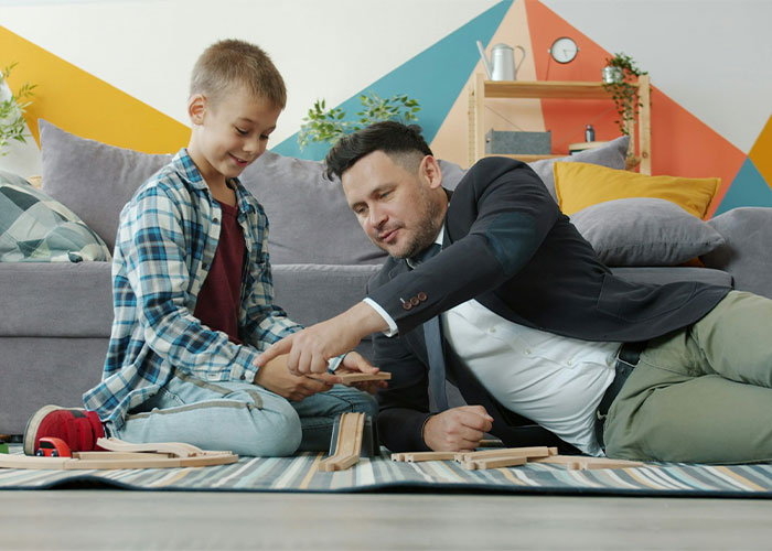 A man playing with a child on the floor with toy trains, symbolizing being with children. A man playing with a child on the floor with toy trains, symbolizing being with children.