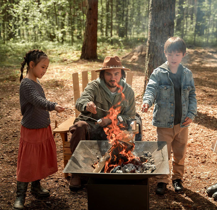 Man, children, and girlfriend cooking marshmallows over a fire, enjoying family time outdoors. Man, children, and girlfriend cooking marshmallows over a fire, enjoying family time outdoors.