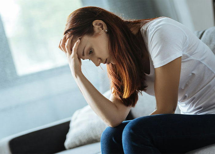 A worried woman with red hair holds her head, contemplating a difficult compromise about her children and relationship. A worried woman with red hair holds her head, contemplating a difficult compromise about her children and relationship.