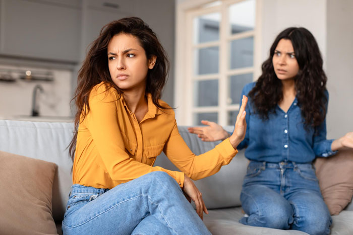 A woman in a yellow shirt looks away from her toxic sis, who appears upset on a sofa. Sis is infertile. A woman in a yellow shirt looks away from her toxic sis, who appears upset on a sofa. Sis is infertile.