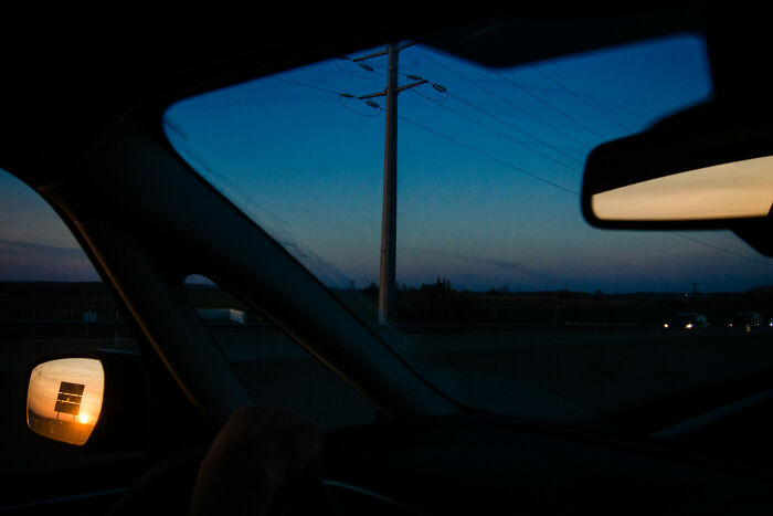 Driving at dusk, a sunset reflects in the side mirror, a striking image from the street photography awards.