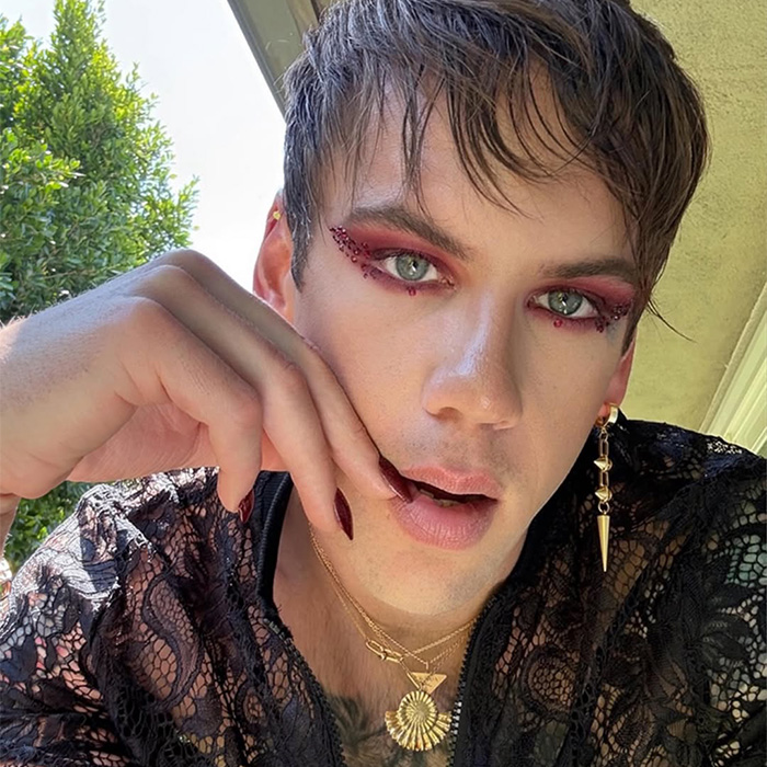 Rock star emerging unrecognizable after coming out as gay, wearing heavy makeup and a lace top.