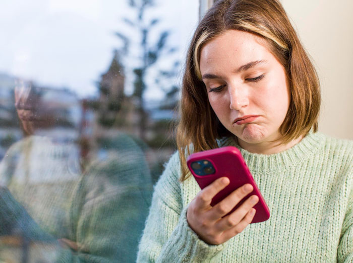 A young woman with a sad expression holding a phone, reflecting on a TikToker's goodbye video. A young woman with a sad expression holding a phone, reflecting on a TikToker's goodbye video.