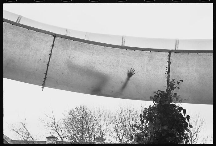 A silhouetted hand pressed against a translucent tunnel or slide from below, a striking and artistic piece of street photography.