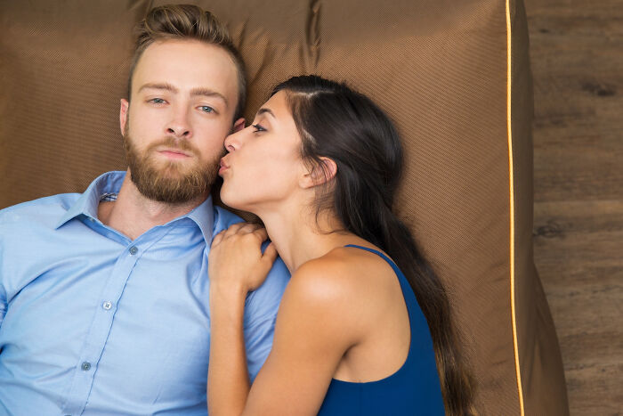 A woman kisses an unsmiling man on the cheek, reflecting on reasons people became affair partners.
