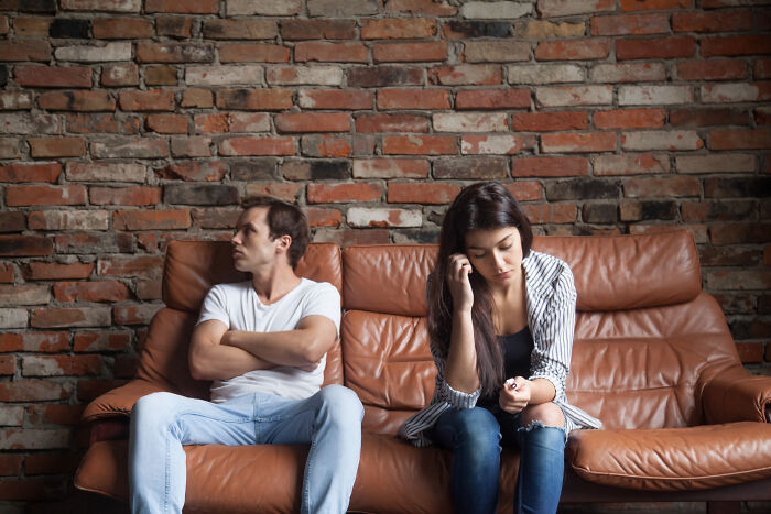 A man and a woman sitting on opposite ends of a sofa, facing away from each other, illustrating affair partners issues.