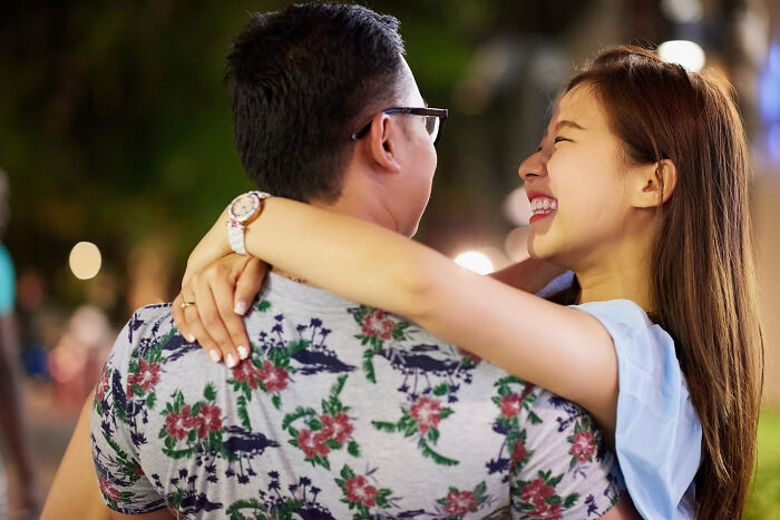 A happy couple embraces outdoors at night, with the woman laughing, illustrating affair partners' complex emotions.